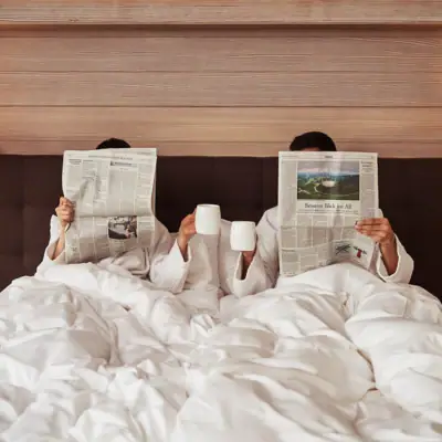 Ein Paar im Bett liest Zeitungen und trinkt Kaffee.