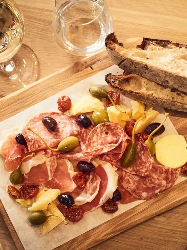 Eine Platte mit Fleisch und Käse, begleitet von Brot und Weingläsern.