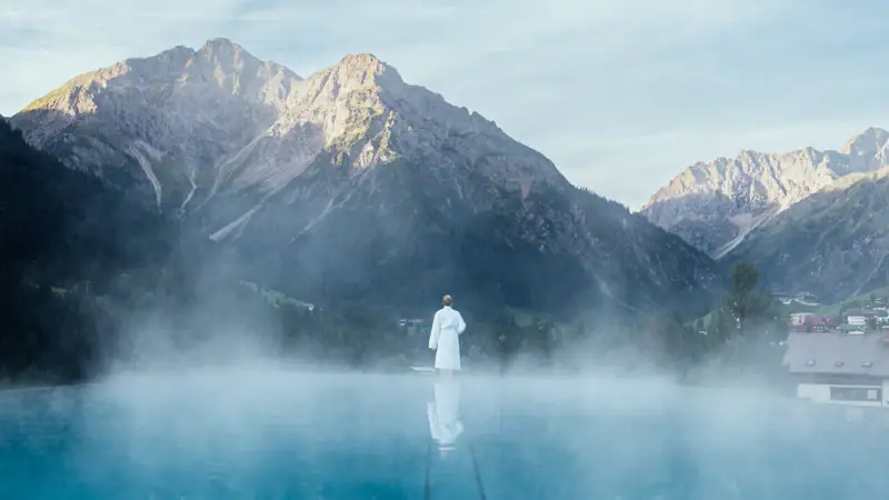 Eine Person steht in einem Wasserbecken mit Bergen im Hintergrund.