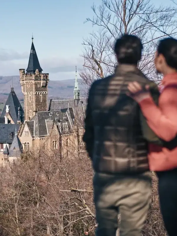 Ein Mann und eine Frau stehen auf einem Hügel und blicken auf ein Schloss.