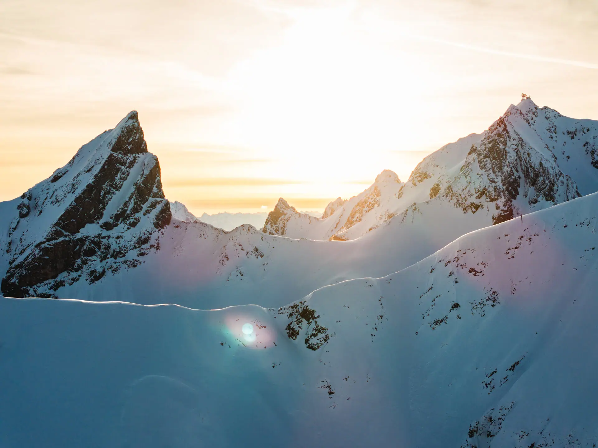 Verschneite Berge mit strahlender Sonne im Hintergrund.