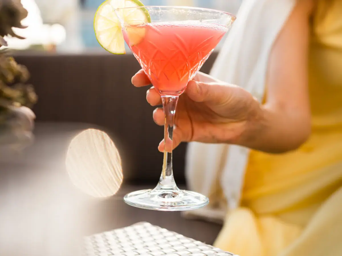 Drink A-ROSA Sylt Eine Frau hält ein Glas mit einem rosa Cocktail auf einer Terrasse.