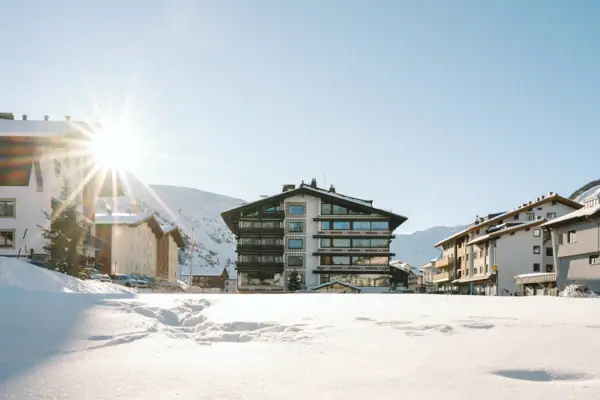 Schneebedeckter Boden mit Gebäuden und Bergen im Hintergrund.