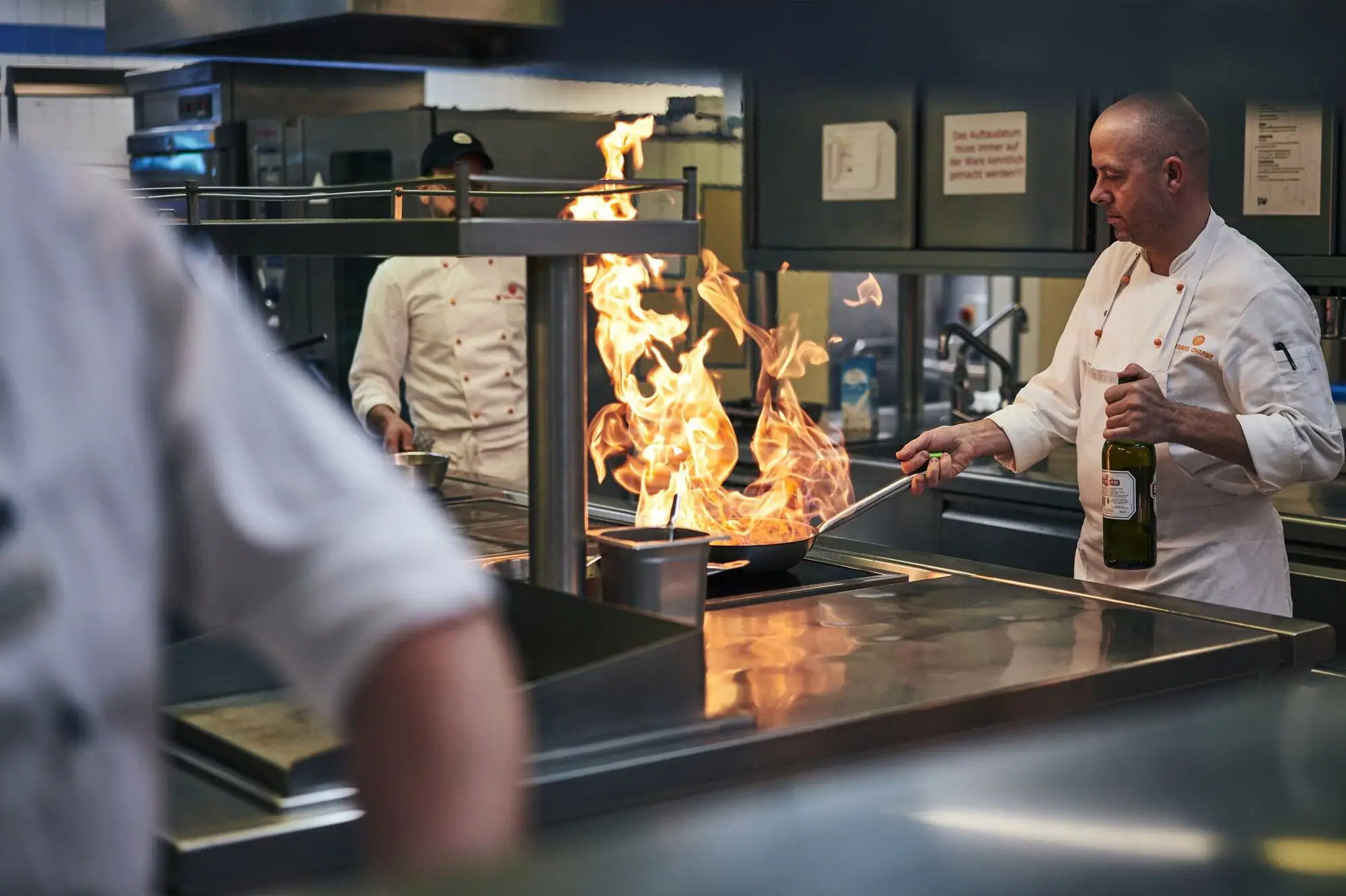 Gastronomie Kurhaus Binz Ein Koch in einer Küche beim Zubereiten von Speisen mit hohen Flammen in einer Pfanne.