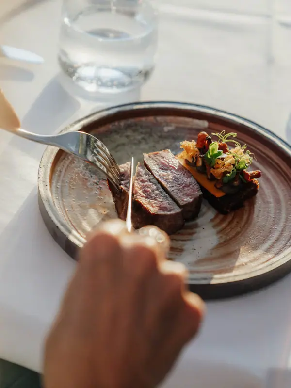 Eine Person schneidet Fleisch auf einem Teller.