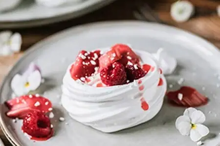 Meringue-Nester Ein Teller mit Dessert, verziert mit Beeren und Sahne, auf einem Tisch.