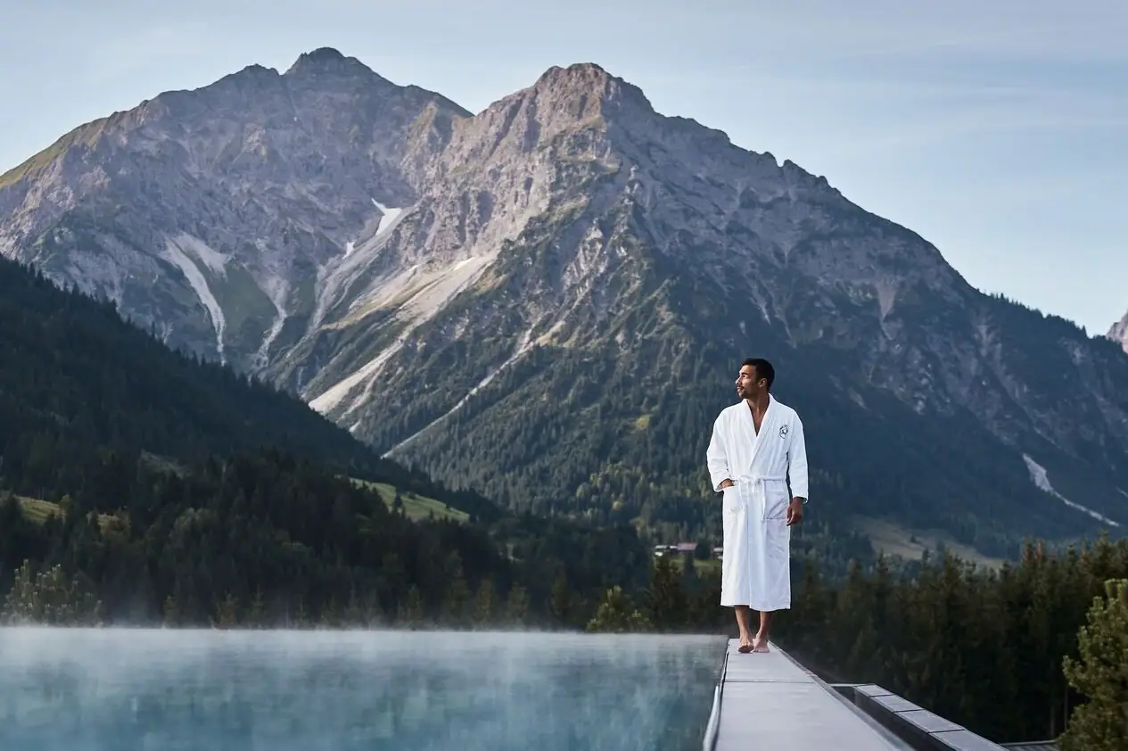 Mann am Pool Ein Mann steht auf einem Steg mit einem Berg im Hintergrund.