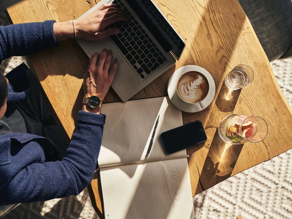 Tagung A-ROSA Kleinwalsertal Eine Person benutzt einen Laptop auf einem Tisch und neben ihm liegt ein großes Notizbuch, ein Kaffee und ein Handy.