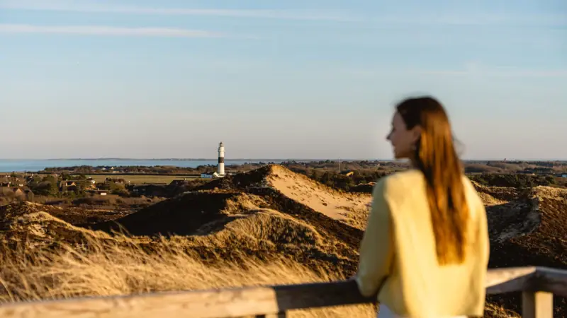 Sylt Düne Eine Frau steht auf einem Zaun und blickt auf einen Leuchtturm.