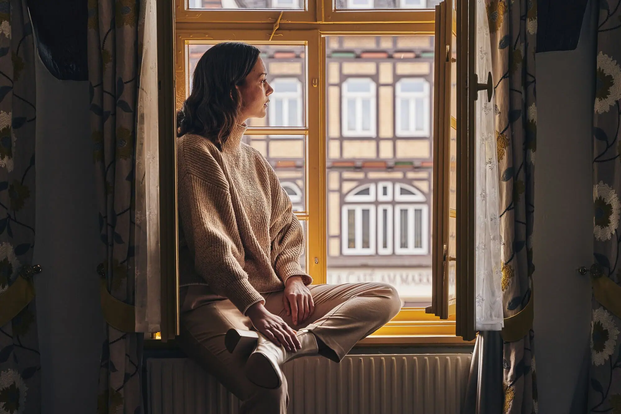 Zimmerausblick Eine Frau sitzt auf einer Fensterbank und blickt aus dem Fenster.