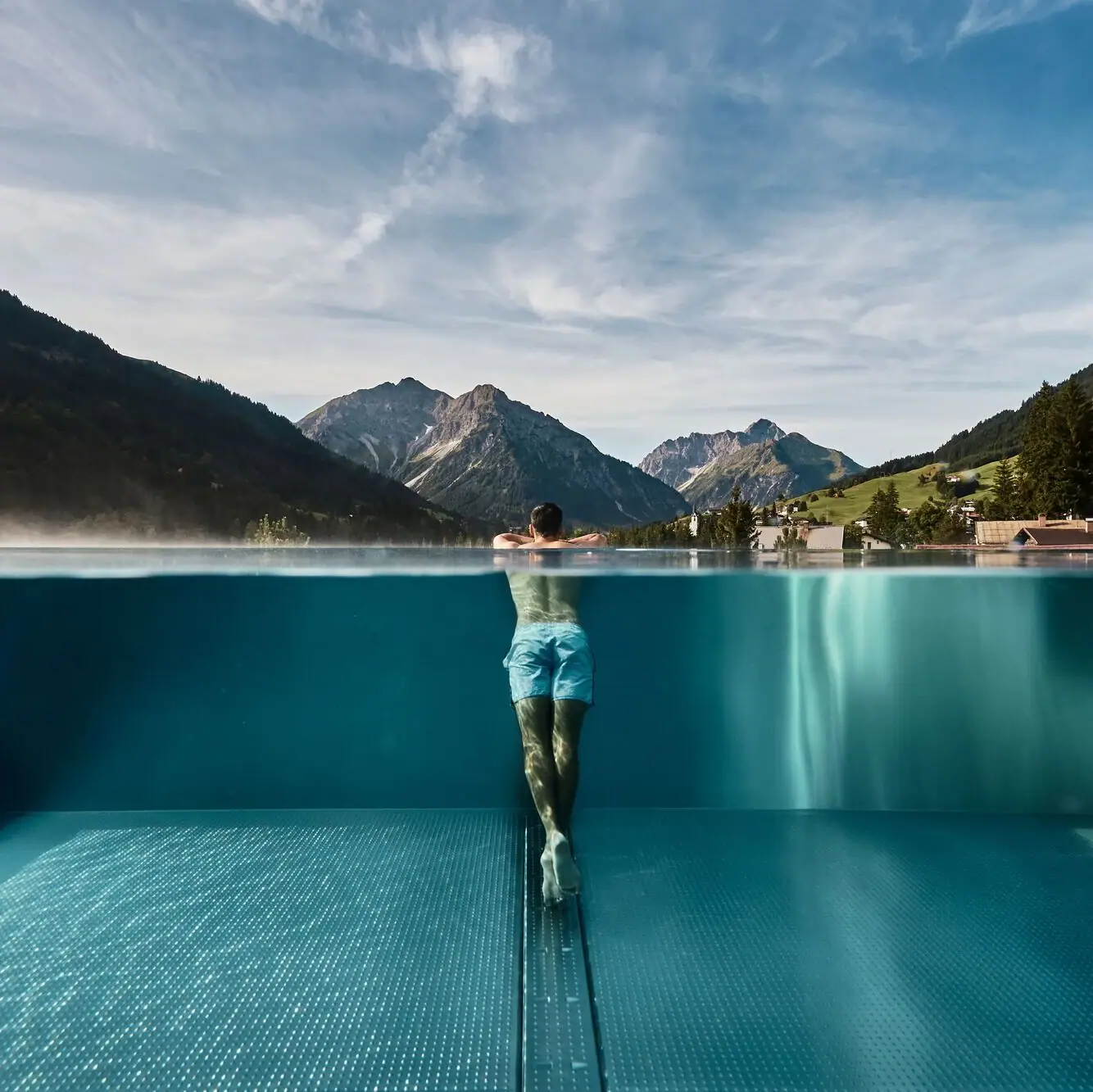 Outdoor Infinity Pool im Ifen Hotel Kleinwalsertal Ein Mann in einem Infinity Pool unter freiem Himmel mit Bergen im Hintergrund.