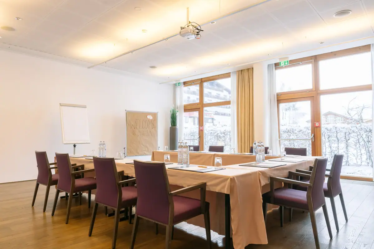 Tagungsraum A-ROSA Kleinwalsertal Ein Tagungsraum mit mehreren Tischen und Stühlen in U-Formsowie einer Pinnwand und einem Flipchart im Hintergrund.