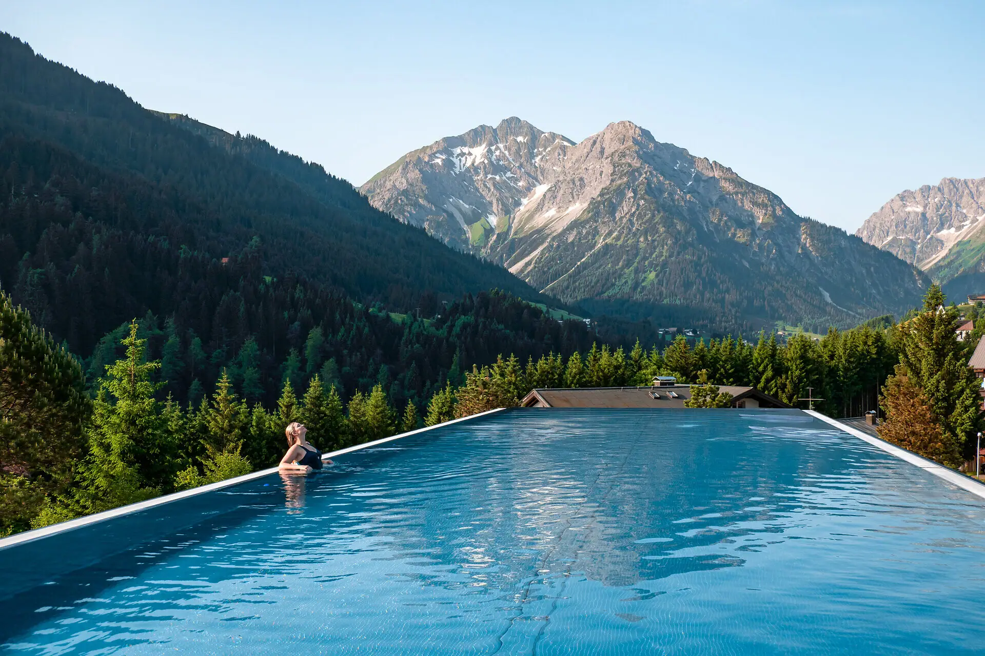 Außenpool Ifen Hotel Eine Frau in einem Pool mit Bergen im Hintergrund.