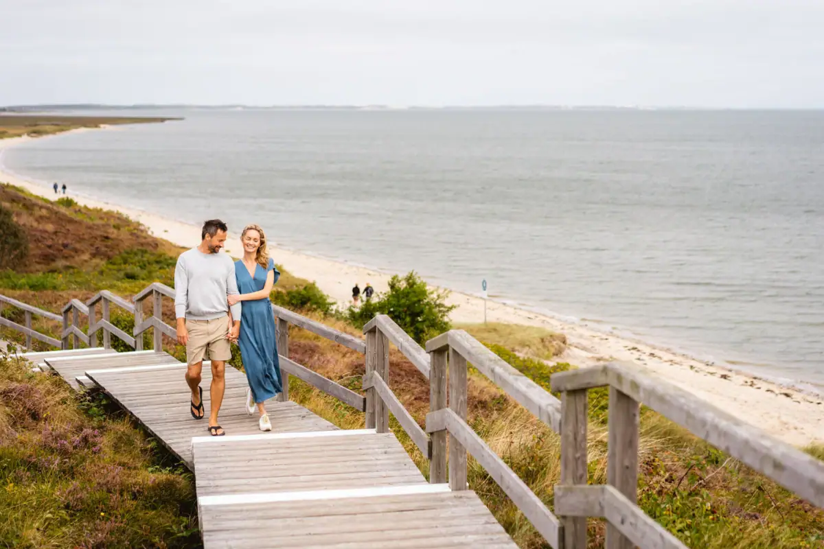 Ein Mann und eine Frau gehen auf einem Holzsteg in der Nähe eines Strandes.