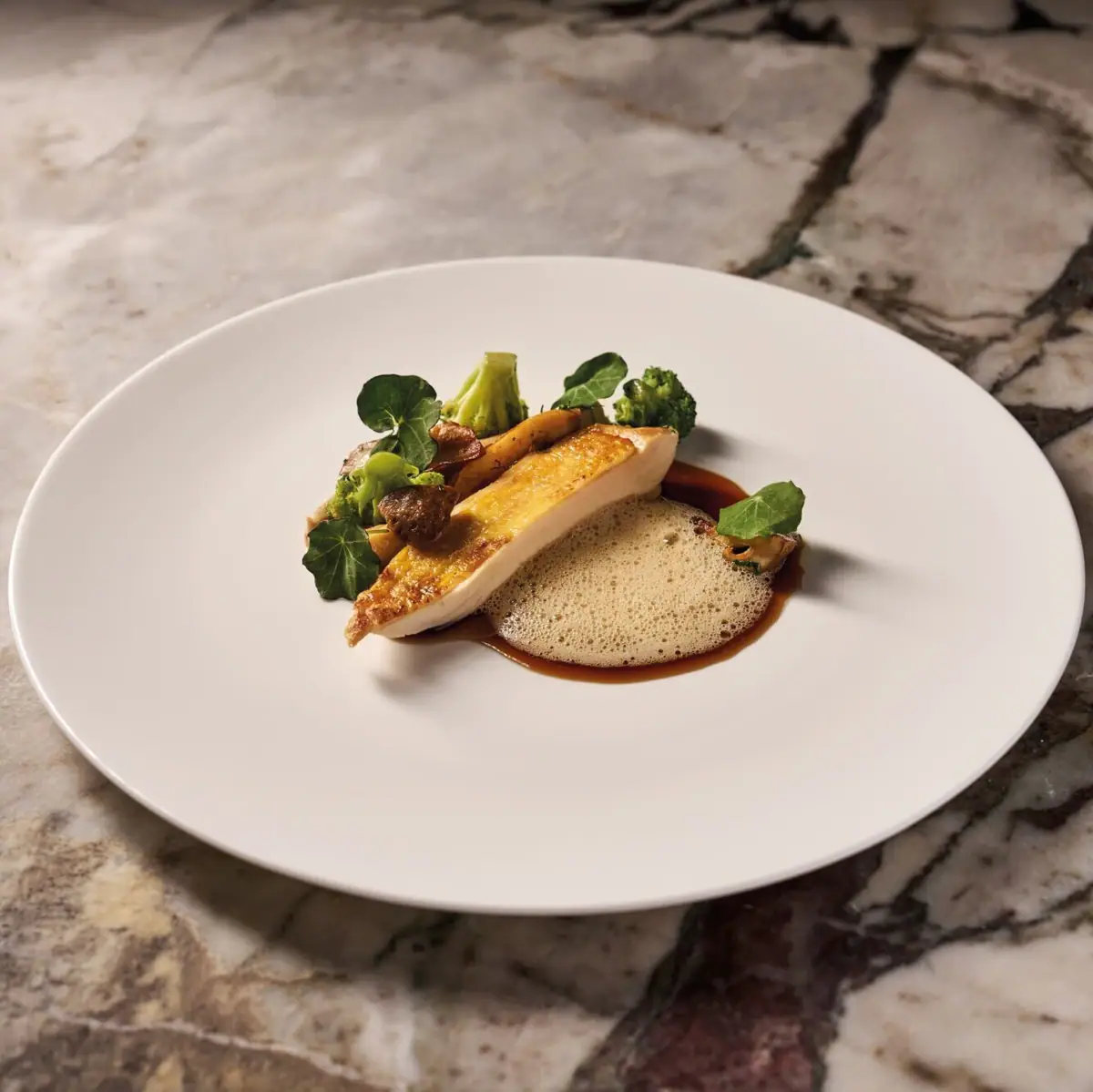 Fine-Dining Erlebnis im Restaurant Ein kunstvoll angerichtetes Gericht auf weißem Teller, welcher auf marmoriertem Untergrund steht.