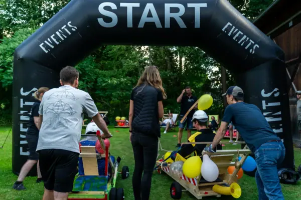 Seifenkisten-Spektakel Eine Gruppe von Menschen in einem Feld mit einem schwarzen Torbogen.