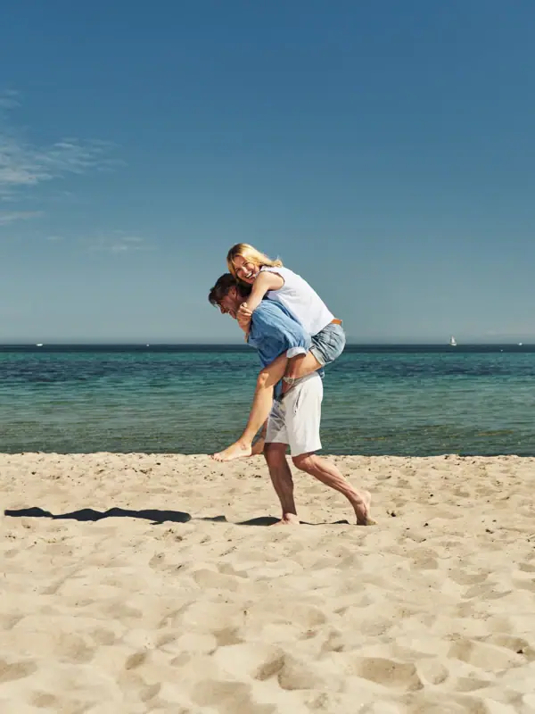 Ein Mann trägt eine Frau auf seinem Rücken am Strand.