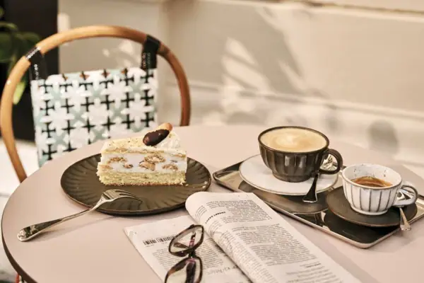 Kaffeehausflair und buntes Treiben Ein Tisch mit einem Kaffee, einem Stück Torte, einer Zeitung und Lesebrille.