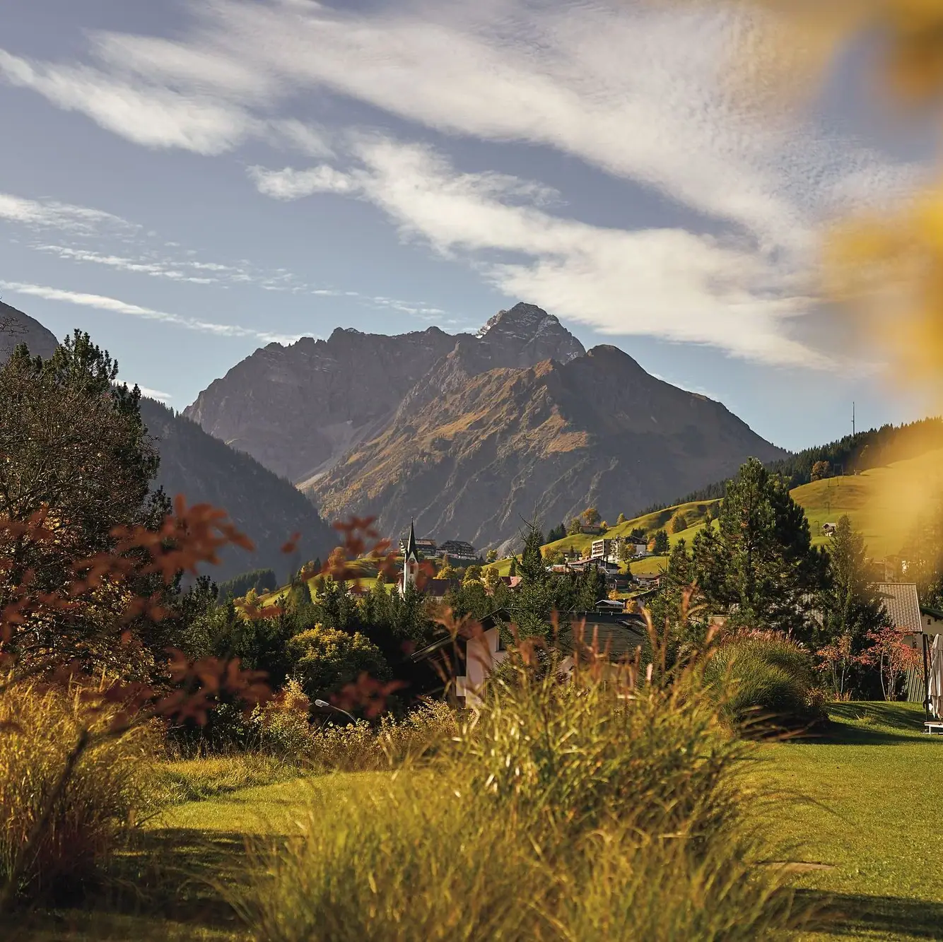 Aktivitäten im Kleinwalsertal Herbstliche Landschaft mit Berg im Hintergrund, umgeben von Gras und vereinzelten Bäumen unter einem bewölkten Himmel.