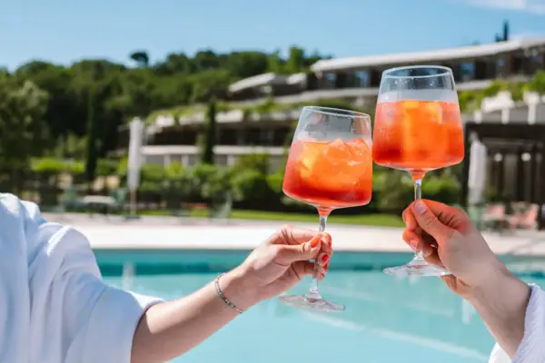 Poolbar im A-ROSA Gardasee Hände halten zwei mit Aperol und Eis gefüllte Gläser.