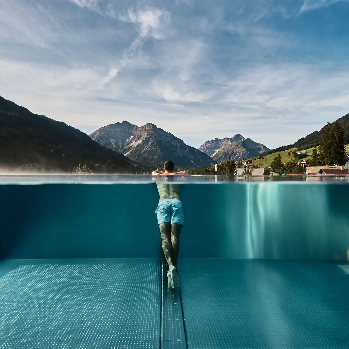Ein Mann schwimmt in einem Pool mit Bergen im Hintergrund.