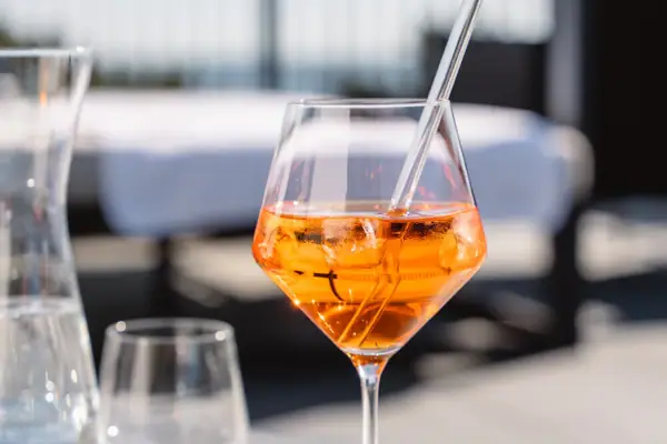 Aperol mit Strohhalm Ein Glas mit orangener Flüssigkeit und Eis auf einem Tisch.