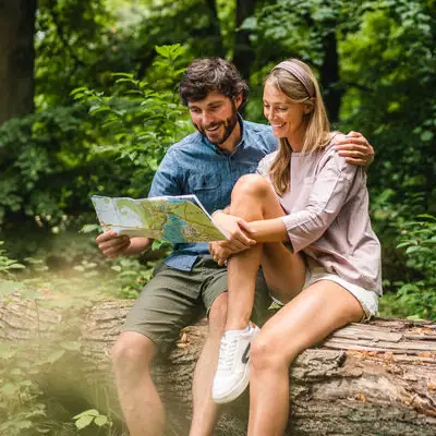 Ein Mann und eine Frau sitzen auf einem Baumstamm und betrachten eine Karte im Freien.