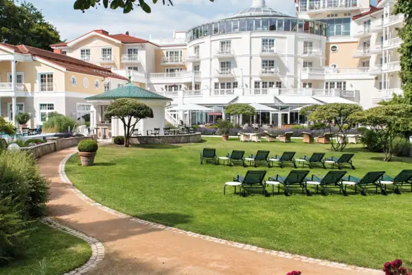 A-ROSA Heringsdorf Außengarten Liegestuhl im Garten mit Bäumen und klarem Himmel im Hintergrund.