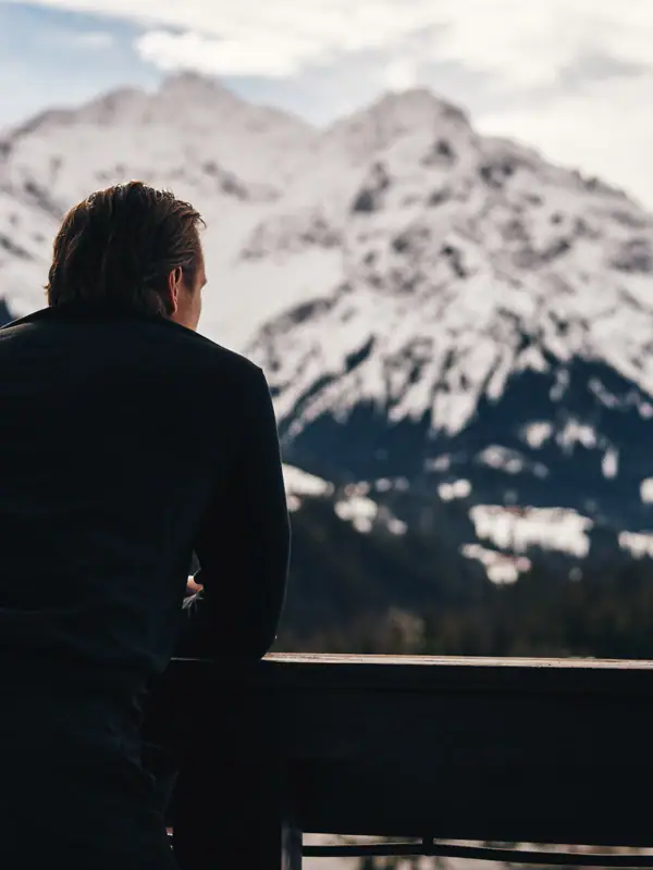 Ausblick Ein Mann lehnt an einem Geländer mit Blick auf einen verschneiten Berg.