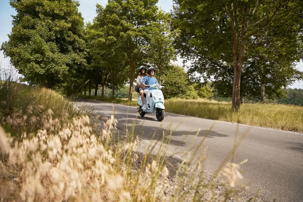 paar-trip-fahren-roller-durch-allee-strandidyll-heringsdorf Ein Mann und eine Frau fahren auf einem Roller eine Straße entlang.