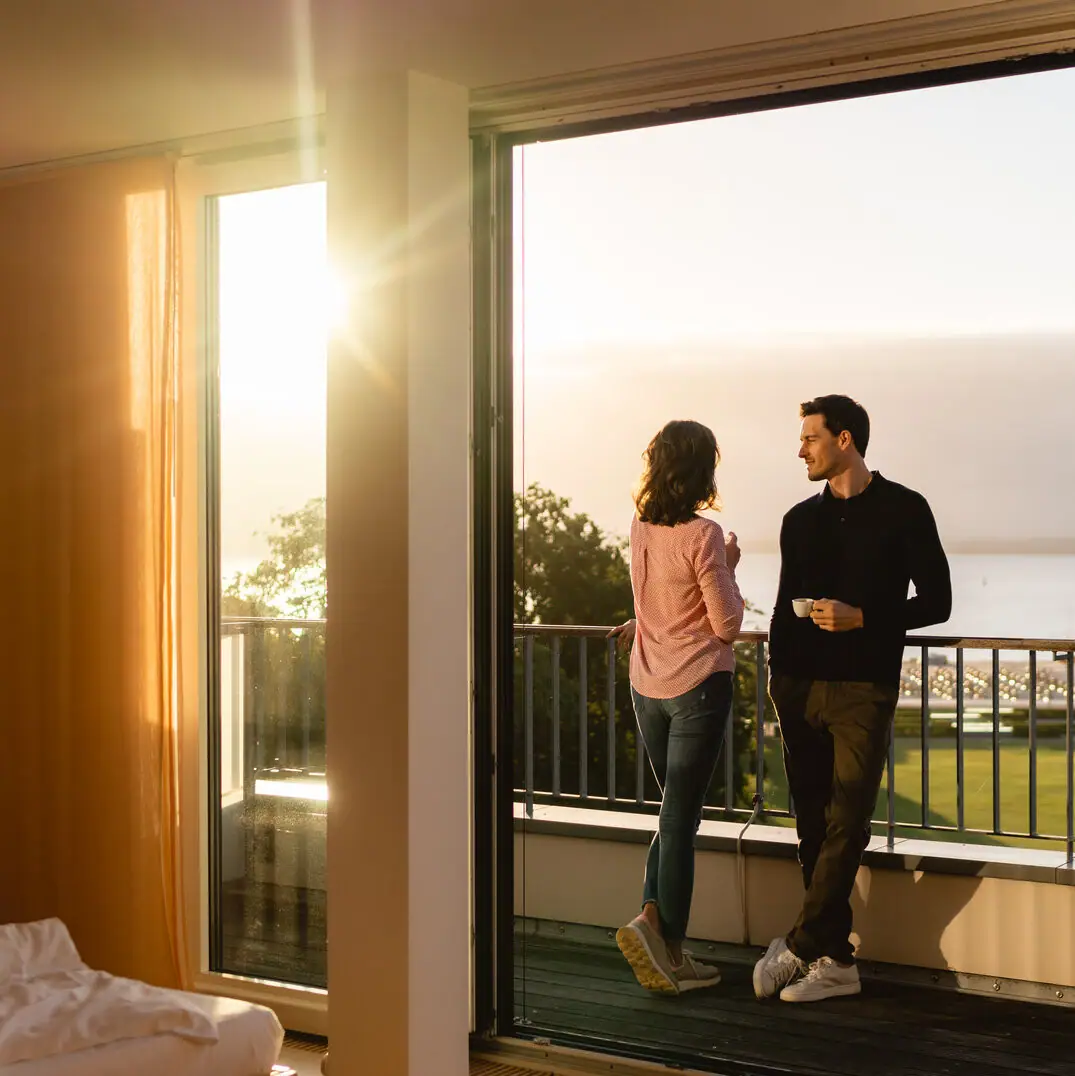 Zimmer & Suiten in Travemünde Ein Mann und eine Frau stehen auf einem Balkon und schauen aus einem Fenster.
