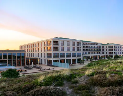 A-ROSA Sylt Großes Gebäude mit Rasen und Stühlen im Freien.