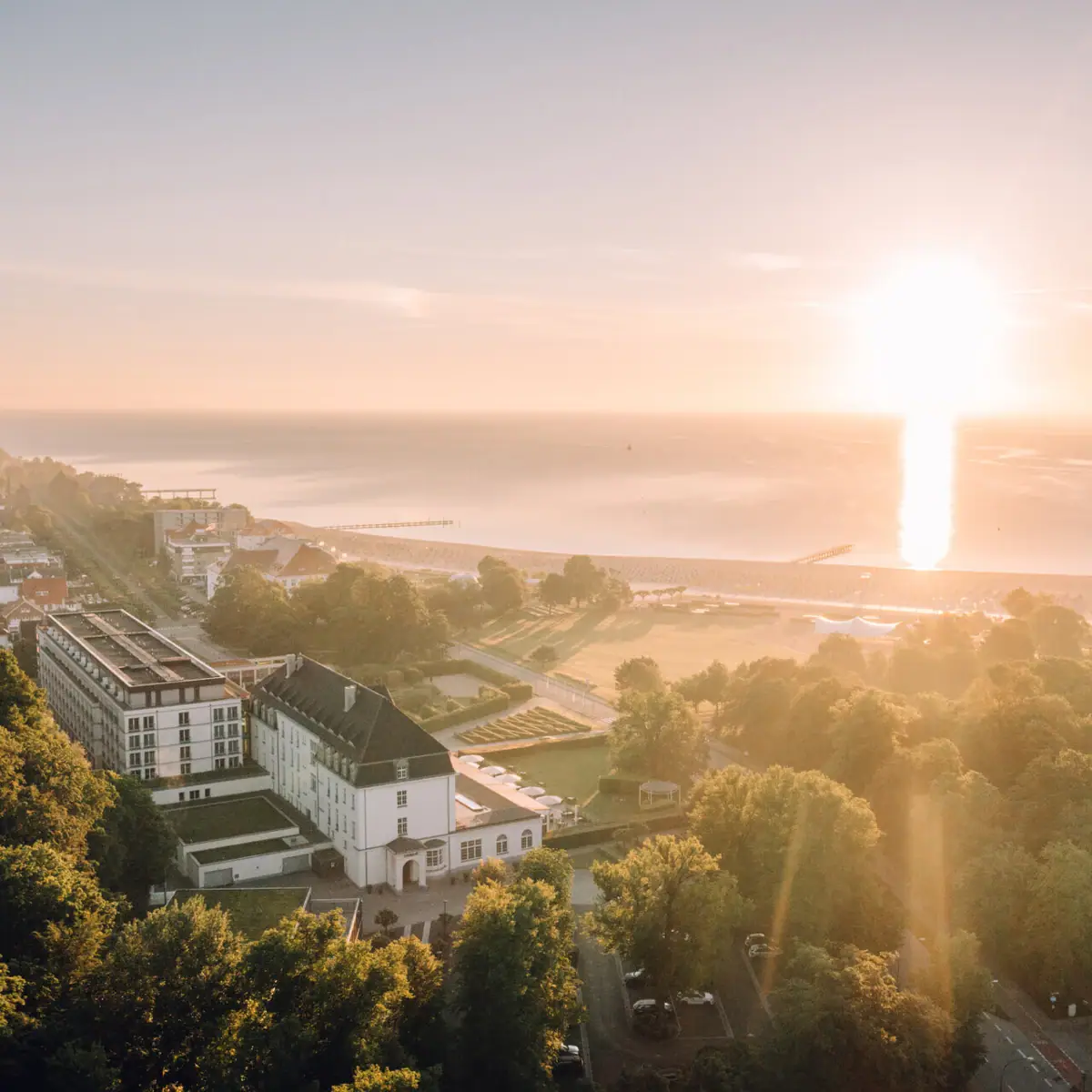 A-ROSA Travemünde Eine Stadt mit Bäumen und einem Gewässer bei Sonnenaufgang.