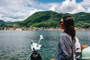 Gardasee Eine Frau sitzt auf einem Roller und blickt auf ein Gewässer.