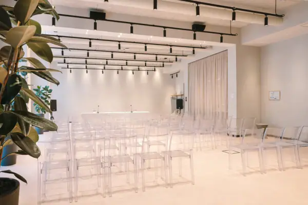 Creavista im A-ROSA Gardasee Ein Tagungsraum mit transparenten Stühlen und einem Pult vorne. Das Pult ist mit Mikrofonen ausgestattet. Außerdem stehen am Rand jeweils Lautsprecher.