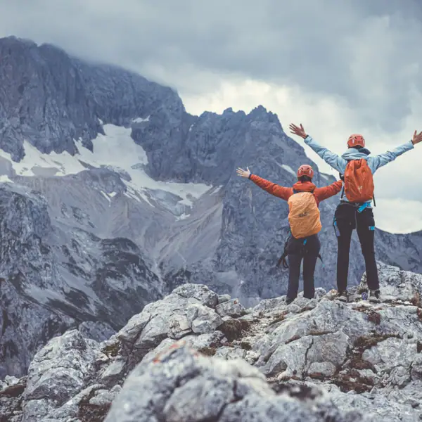 Zwei Personen stehen mit erhobenen Armen auf einem Felsen.