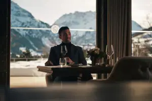 Kilian Stuba Restaurant Ein Mann sitzt an einem Tisch mit Weingläsern und Bergen im Hintergrund.