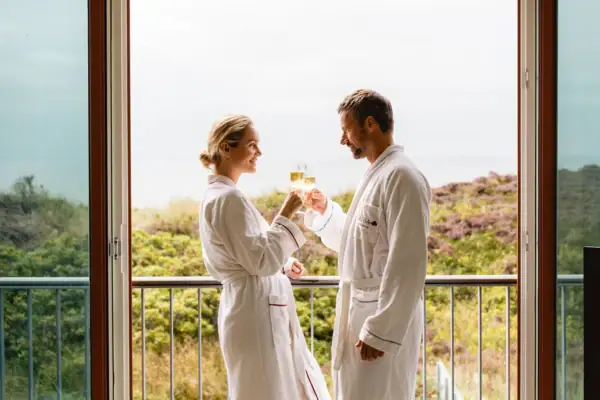 Ein Mann und eine Frau in weißen Bademänteln halten Gläser mit Champagner.