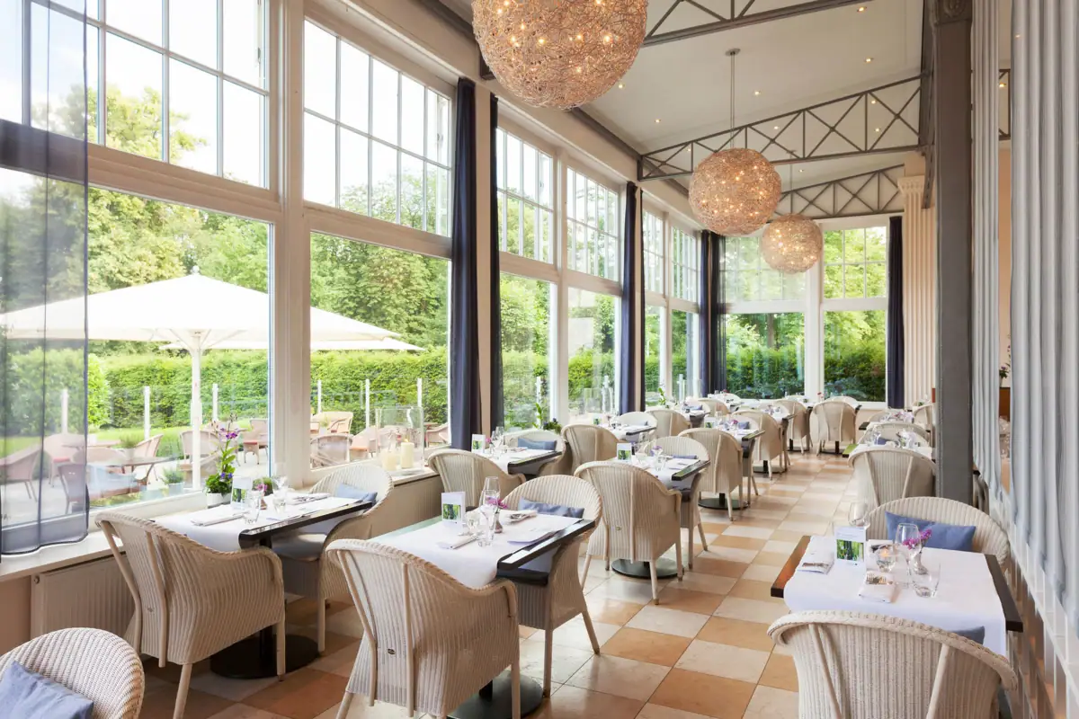 Wintergarten A-ROSA Travemünde Das Wintergarten-Restaurant im A-ROSA Travemünde mit vielen hellen Korbsesseln und eingedeckten Tischen.