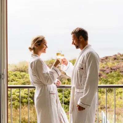 Ein Mann und eine Frau in weißen Bademänteln halten Champagnergläser.