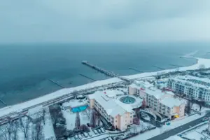A-ROSA Ostseehotel Kühlungsborn Schneebedeckter Strand mit Gebäuden und einem Pier im Winter.