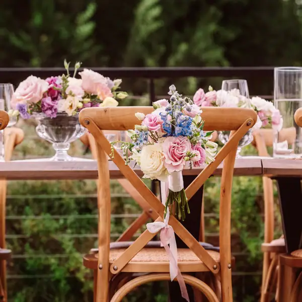 Blumendekorierte Hochzeitsstühle Holzstühle einer Hochzeitstafel, mit kleinen Sträußen aus Rosen und Bändern festlich geschmückt.