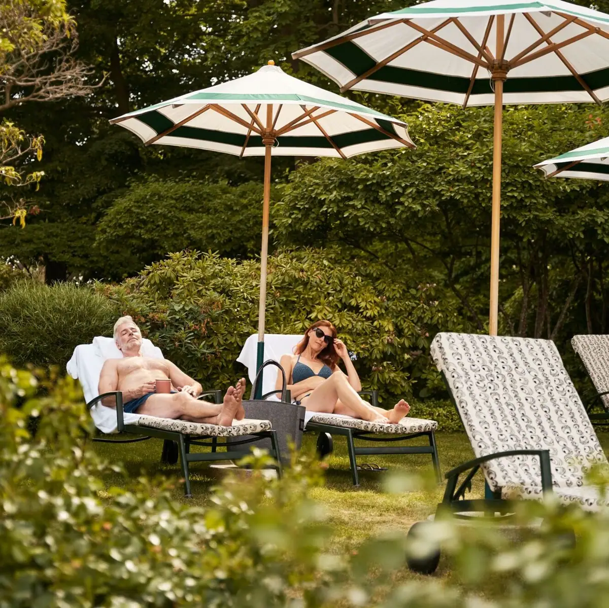 Ein Mann und eine Frau sitzen auf Liegestühlen unter Sonnenschirmen.
