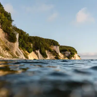 Körper aus Wasser mit Klippe und Bäumen im Hintergrund.
