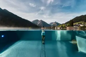 Infinitypool Eine Person steht in einem Pool mit Bergen im Hintergrund.