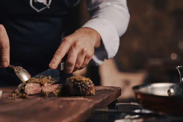 Person schneidet Fleisch auf einem Schneidebrett.
