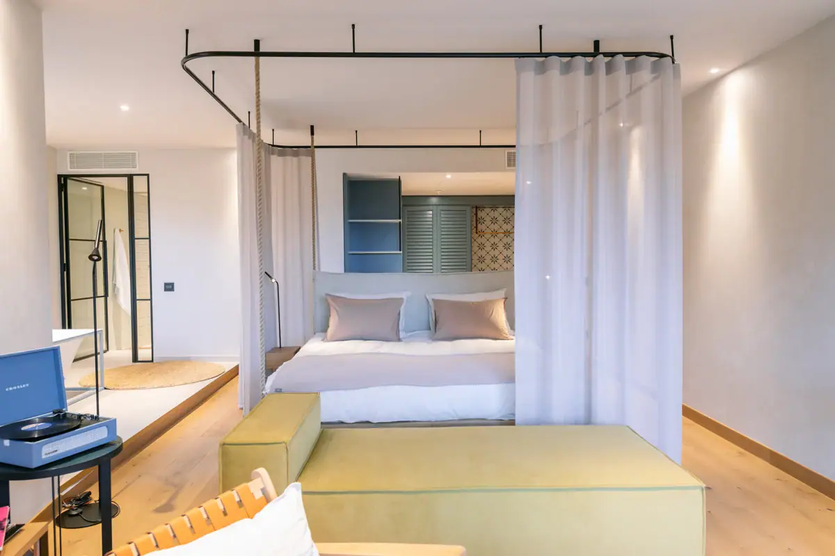 Juniorsuite mit Badewanne Ein Bild von einer Juniorsuite mit einem Bett. Um das Bett ist ein Vorhang, den man zuzuiehen kann. Vor dem Bett steht eine Couch. Im Hintergrund sieht man eine freistehende Badewanne.