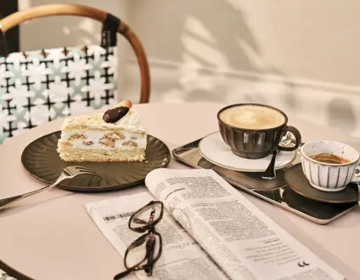 Kaffeezeit auf der Terrasse Ein Tisch mit einem Kaffeegedeck, einem Stück Kuchen und einer Zeitung