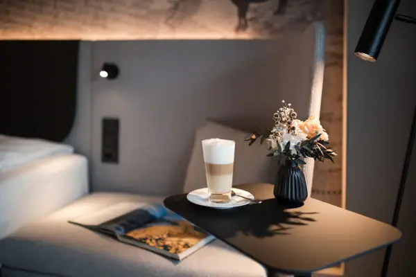 Zimmer Ein Tisch mit einem Getränk und einer Vase mit Blumen darauf.