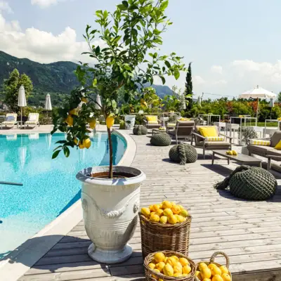Firmenfeiern im A-ROSA Gardasee Der Gartenpool vom A-ROSA Gardasse dekoriert mit einem Baum und Stühlen sowie Körben gefüllt mit Zitronen.